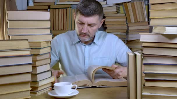 Un uomo barbuto legge un libro in biblioteca — Video Stock