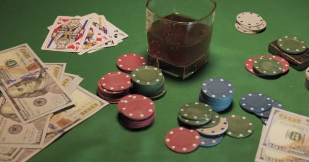 Чипсы, карты, стакан виски и деньги на зеленом игровом столе — стоковое видео