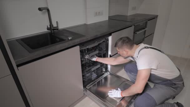 Un riparatore professionista in tuta da lavoro controlla una lavastoviglie domestica in cucina — Video Stock