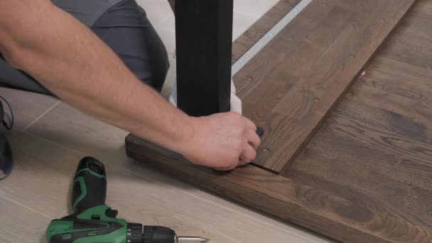 Строитель в комбинезоне винтит ножки стола с помощью отвертки — стоковое видео