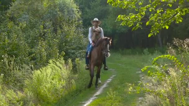 Cowboy and his daughter on horseback on a forest lawn — Stock Video