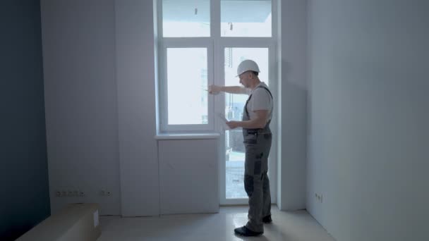 Um construtor em uniforme verifica o tamanho e a qualidade da instalação da janela em um novo apartamento — Vídeo de Stock
