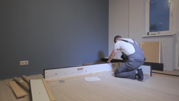 Строитель в рабочем комбинезоне собирает кровать в новой квартире — стоковое видео