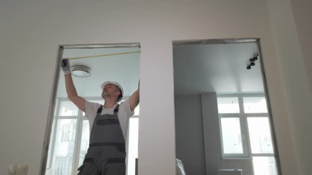 Строитель в рабочей форме проверяет размер и качество дверных проемов в новой квартире — стоковое видео