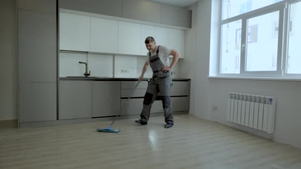 Ein fröhlicher Arbeiter in Uniform wäscht den Boden in einer neuen Wohnung — Stockvideo