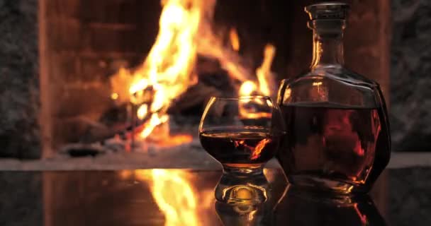 Μπουκάλι και ποτήρι με ουίσκι ή κονιάκ στο φόντο της φωτιάς στο τζάκι — Αρχείο Βίντεο