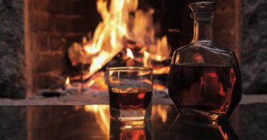 Şöminenin arka planında viski ya da konyak olan şişe ve bardak.
