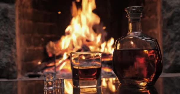 Flasche und Glas mit Whiskey oder Cognac auf dem Hintergrund des Feuers im Kamin — Stockvideo