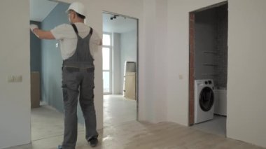Çalışan üniformalı bir müteahhit, yeni bir apartmanın kapılarının büyüklüğünü ve kalitesini kontrol eder.