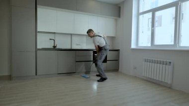 Üniformalı neşeli bir işçi yeni bir dairede yerleri yıkıyor.