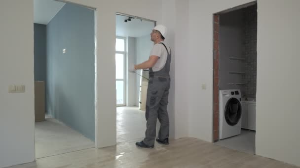 Een bouwer in uniform werkt controleert de grootte en kwaliteit van de deuropeningen in een nieuw appartement — Stockvideo