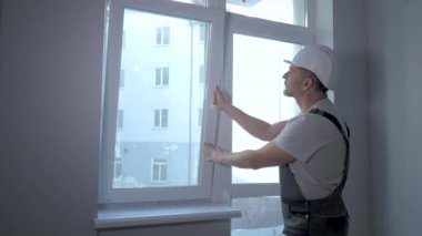 Üniformalı bir müteahhit yeni bir dairede pencere kurulumunun büyüklüğünü ve kalitesini kontrol eder