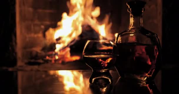 Palack és üveg whiskyvel vagy konyakkal a kandallóban a tűz hátterében — Stock videók
