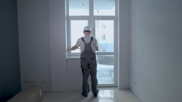 Строитель в форме проверяет размер и качество оконной установки в новой квартире — стоковое видео