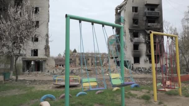 Crianças balançam contra o pano de fundo de um edifício residencial destruído como resultado de um bombardeio pelo exército russo — Vídeo de Stock
