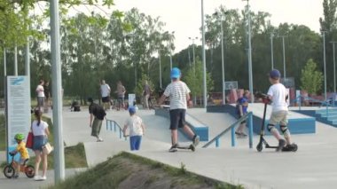 KYIV, UKRAINE - 13 Haziran 2022: Gençler bir yaz günü açık hava kaykay parkında scooter ve bisiklet sürerler. Spor faaliyetleri ve modern gençlik kültürü kavramı.