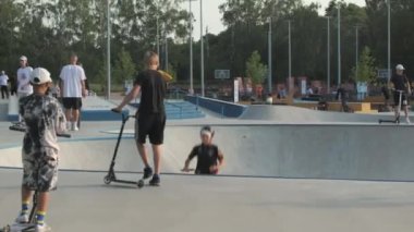 KYIV, UKRAINE - 13 Haziran 2022: Gençler bir yaz günü açık hava kaykay parkında scooter ve bisiklet sürerler. Spor faaliyetleri ve modern gençlik kültürü kavramı.