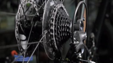 Bisiklet tekerleği teçhizatı ve zincir hareket halinde. Motosikletli araba ve kaset, kapatın. Bisiklet tamiri. Bisiklet atölyesi. Bisiklet zincirini ve dişlileri test etmek için döndür