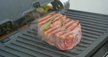 Delicious juicy beef steak with rosemary is cooked on an electric grill. Aged prime rare roast grilling tenderloin fresh marble tenderness beef. Prime beef fry on electric roaster.
