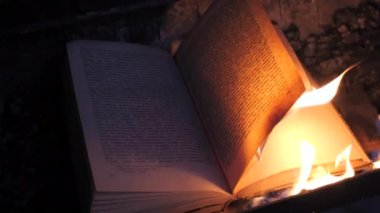 An open book is on fire. Big bright flame, burning paper on old publication in the dark. Book Burning - Censorship Concept, 4K