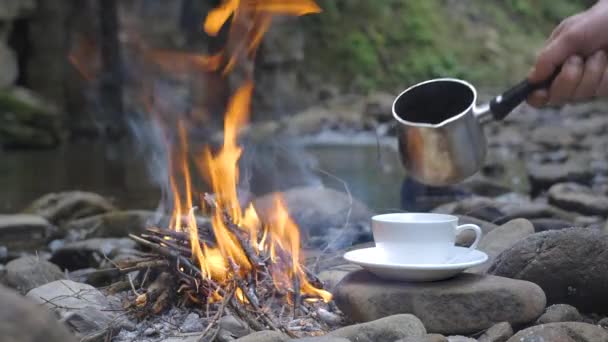 咖啡从咖啡壶倒进杯子里 在一条美丽的河边的火边边吃早餐 旅行概念 — 图库视频影像
