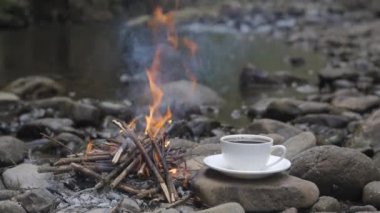 Nehir kıyısındaki ateşin yanında kahve fincanı, yakın plan. Seyahat konsepti. 4k