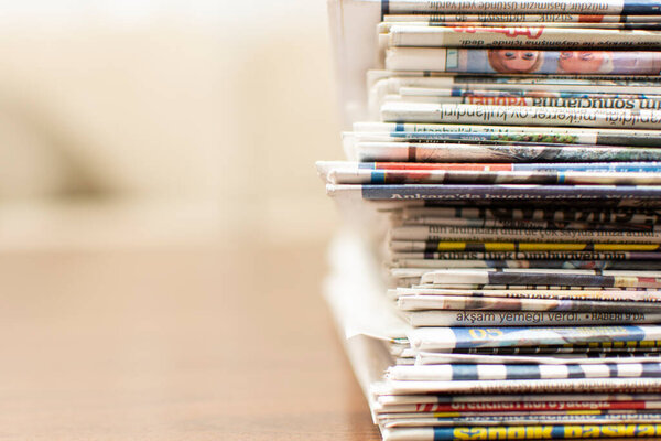 Pile of newspapers lying on the wooden table with blurred background and copy space for text. Close Up of newspapers stack. Journalist concept.