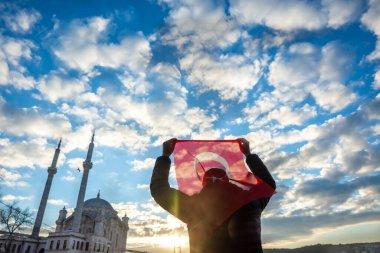 Adam Türk bayrağı taşıyor. İstanbul 'un Ortakoy kentinde Boğaziçi Köprüsü (Türkçe: 15 Temmuz Sehitler Koprusu) ve Sultan Abdulmecid İmparatorluk Camii yakınlarında gün doğumu. Vatanseverlik