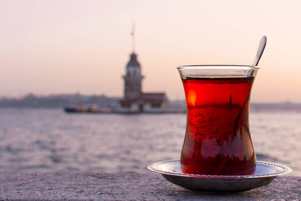 Magnific view of Maiden's Tower (aka Kiz kulesi) at night time on the background and traditional turkish tea on the front. Istanbul attractions.