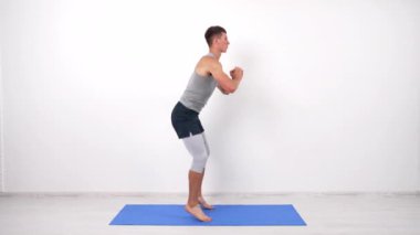 Sporcu adam çömeliyor, spor paspasında zıplıyor, çömeliyor.