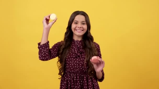 Happy playful girl kid have cookie fun sticking tongue out yellow background, macaroons — Stock Video