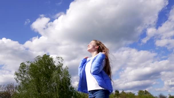 Щаслива дівчина-підліток в осінній куртці насолоджуйтесь сонцем на фоні неба, мотивація — стокове відео