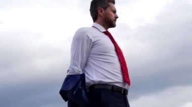 Kendine güvenen sakallı patron, arka planda ceketini çıkarıyor, ofis modasında.