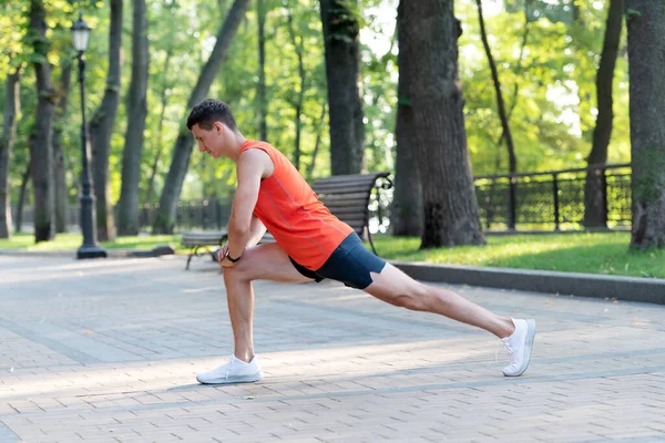 Спортсмен тримає позицію лаунжу, роблячи розтягування рутини під час тренувань на відкритому повітрі в парку, розминка — стокове фото