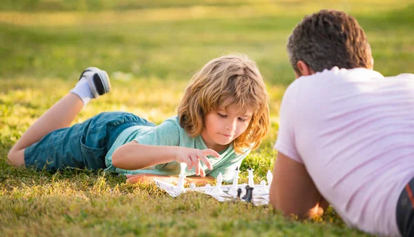 Familia feliz de papá e hijo niño jugando ajedrez sobre hierba verde en el parque al aire libre, táctica — Foto de Stock