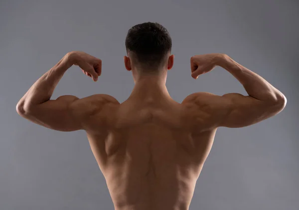 Fit man tylnej tułowia elastyczna mięsień ramienia pokazuje biceps triceps szare tło, zginanie — Zdjęcie stockowe