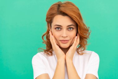 Gülümseyen kızıl saçlı kadın, pürüzsüz tenli, mavi arka planda kıvırcık saçlı, cilt bakımlı.