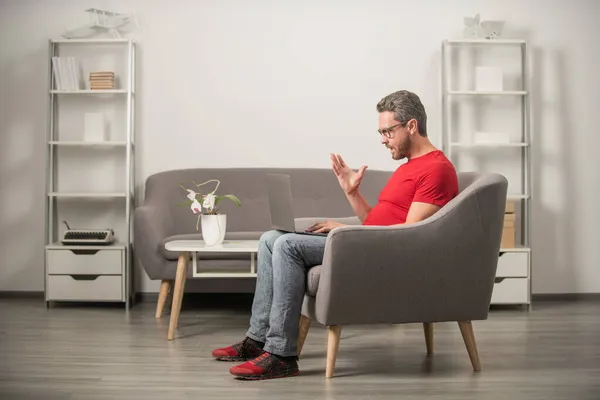 Adult man in glasses working on computer sitting in chair, freelance — Stock Photo, Image