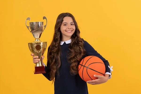 Sonriente niño mantenga pelota de baloncesto y copa campeón sobre fondo amarillo, logro —  Fotos de Stock
