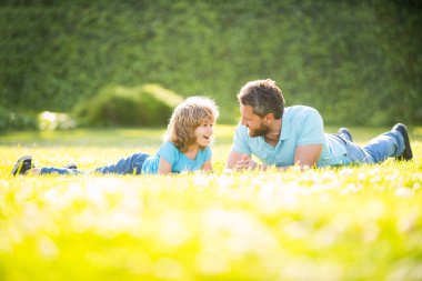 Mutlu baba ve oğul ailesi yaz parkında yeşil çimlerde rahatlar, ebeveynlik yapar.