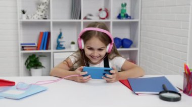 Kulaklıklı mutlu okul kızı sınıfta akıllı telefondan video izleyip para kazanıyor.