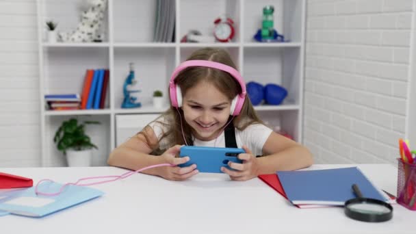 Glad skolflicka i hörlurar titta på video på smartphone i klassrummet, elärande — Stockvideo