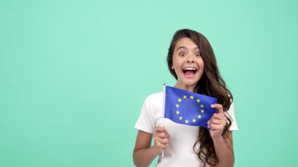 Zaskoczony dziecko machając flagą Unii Europejskiej na niebieskim tle pokazuje kciuk w górę, schengen wizy — Wideo stockowe
