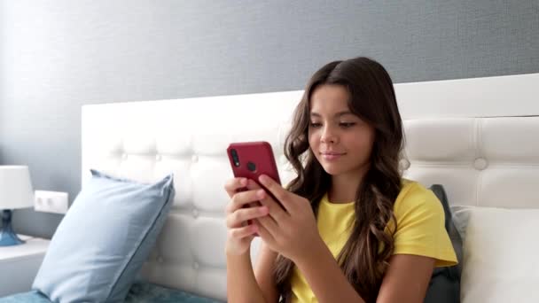 Χαμογελαστό έφηβος κορίτσι δακτυλογράφηση μήνυμα στο κινητό τηλέφωνο στο υπνοδωμάτιο, κινητή τεχνολογία — Αρχείο Βίντεο