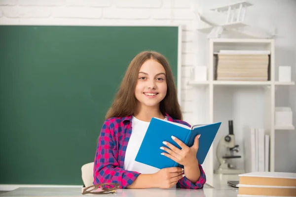 Happy kid sitting with copybook in classroom at blackboard, knowledge — Stock Photo, Image