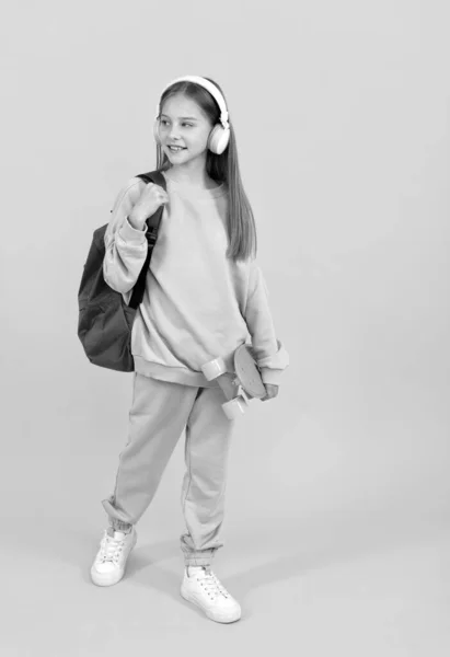 Menina adolescente feliz garoto com mochila escolar e placa de centavo ouvir música em fones de ouvido, tempo de escola. — Fotografia de Stock