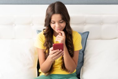 Mutlu kız gülümsemesi yatakta otururken cep telefonuyla konuşuyor, sohbet ediyor.