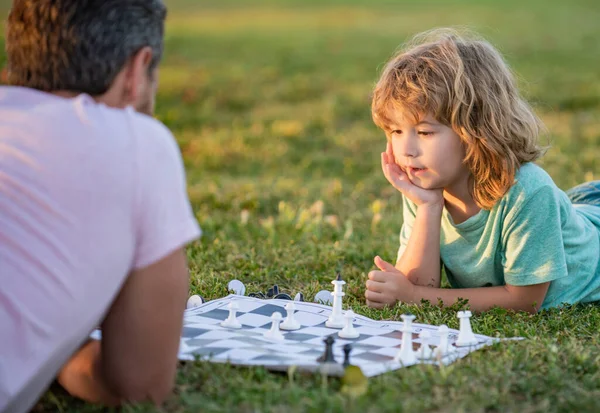 Familia feliz de padres e hijo jugando ajedrez sobre hierba verde en el parque al aire libre, desarrollo de la infancia. — Foto de Stock