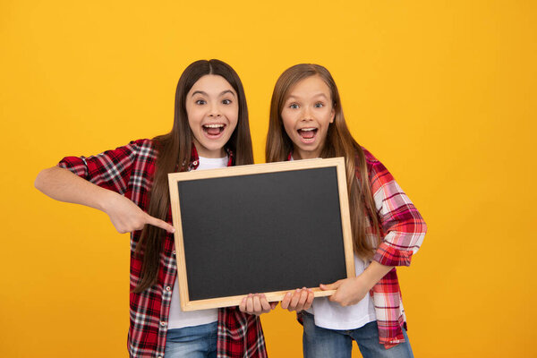 amazed kids in casual checkered point finger on school blackboard for copy space, advertisement