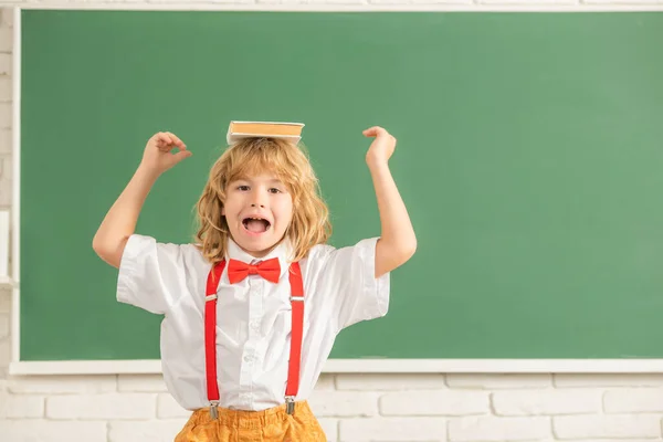 Niño alegre en corbata de lazo en el aula de la escuela con libro, espacio de copia, de vuelta a la escuela — Foto de Stock